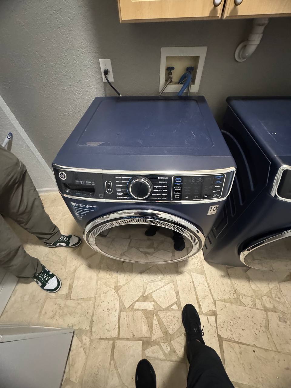GE blue front-load washer pulled out from a utility closet with the water-supply valves and drain hose accessible during an Express Xpert washing machine service call in South Florida